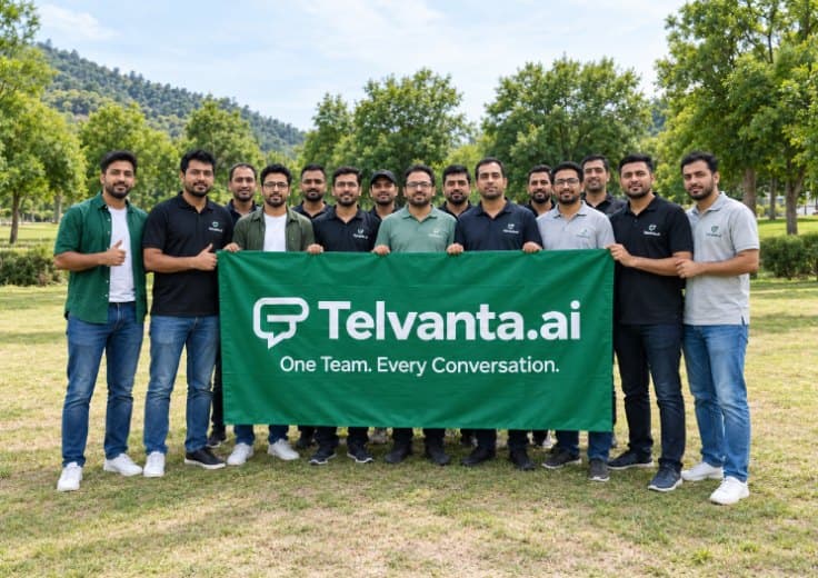 The Telvanta team lined up outdoors on a lawn behind a green banner reading Telvanta.ai — One Team. Every Conversation.
